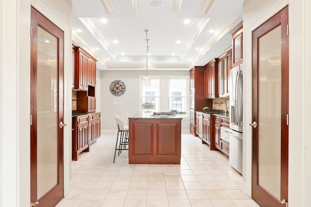 kitchen featuring stainless steel fridge with ice dispenser, a kitchen island, a raised ceiling, a kitchen breakfast bar, and decorative light fixtures