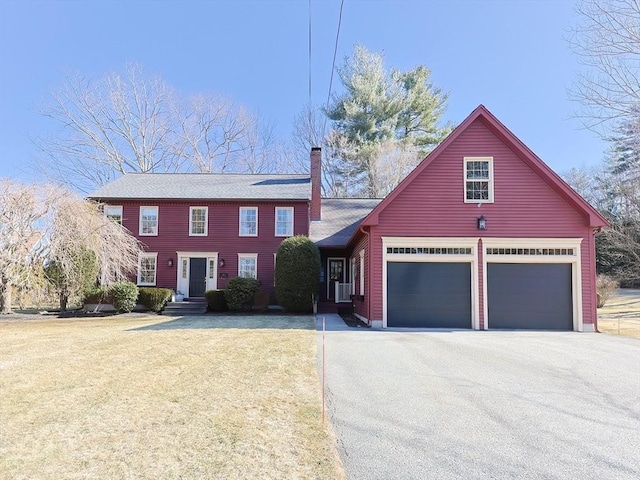 colonial inspired home with a front lawn, an attached garage, driveway, and a chimney