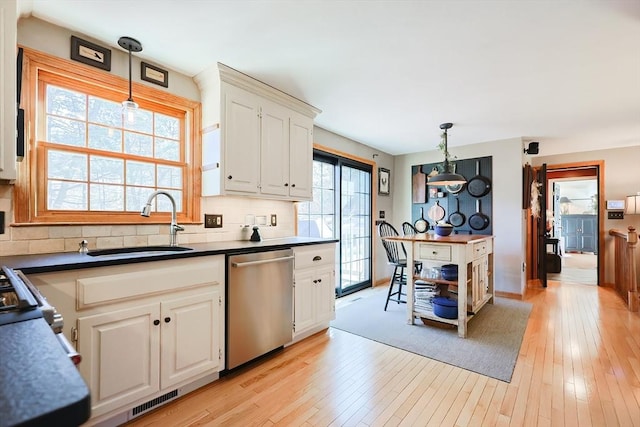 kitchen with dark countertops, light wood-type flooring, decorative backsplash, stainless steel dishwasher, and a sink