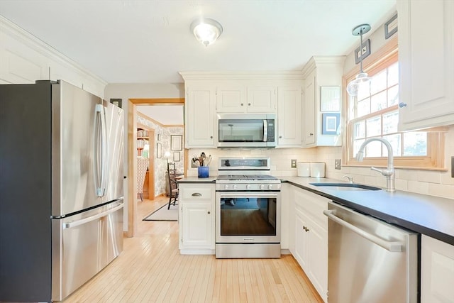 kitchen featuring light wood-type flooring, decorative backsplash, appliances with stainless steel finishes, white cabinetry, and a sink