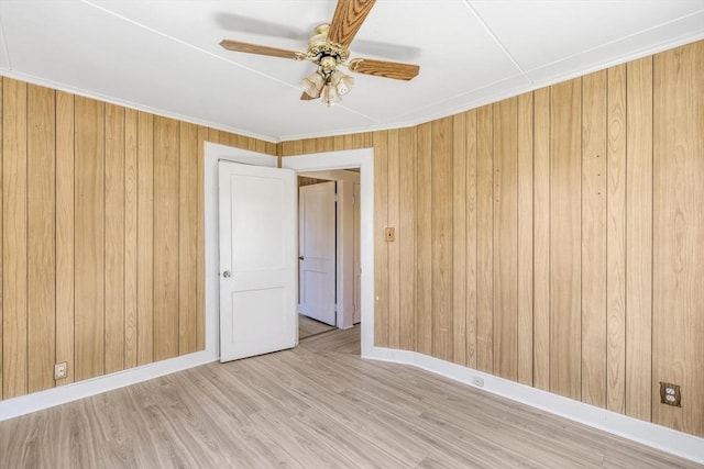 spare room with baseboards, wood walls, wood finished floors, and ceiling fan