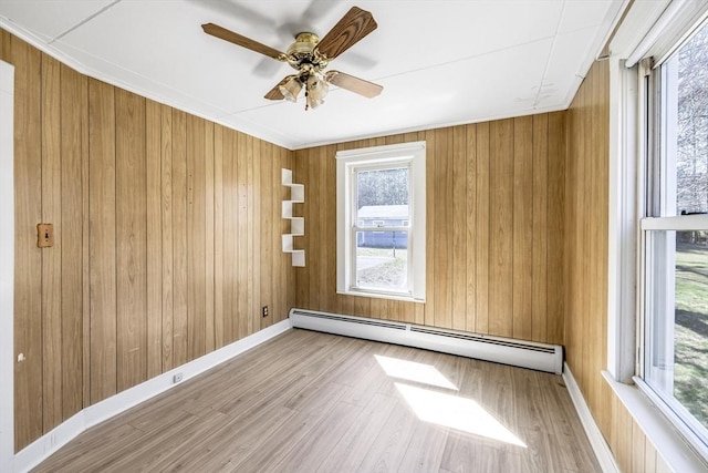 spare room with ceiling fan, a baseboard heating unit, baseboards, wooden walls, and wood finished floors
