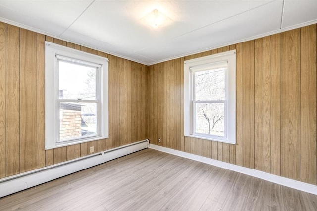 unfurnished room featuring wooden walls, wood finished floors, a healthy amount of sunlight, and baseboard heating