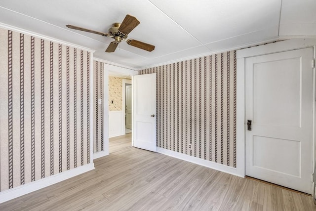 unfurnished bedroom with wallpapered walls, light wood-style floors, baseboards, a ceiling fan, and crown molding