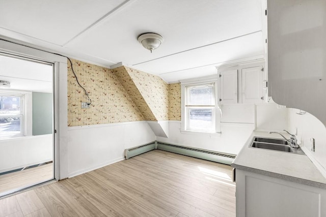 additional living space with a sink, a wainscoted wall, wallpapered walls, light wood-style flooring, and baseboard heating