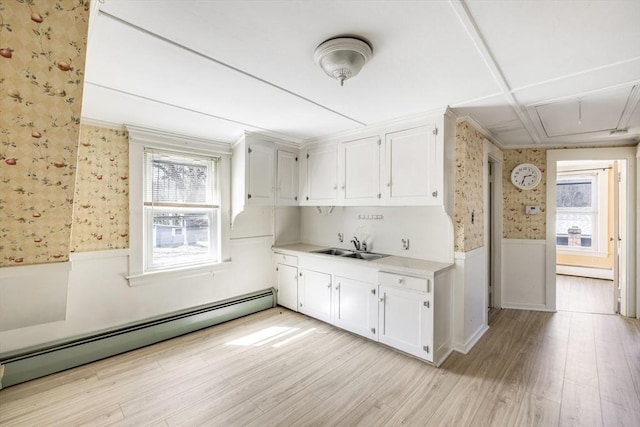 kitchen featuring light wood-style flooring, a baseboard radiator, wallpapered walls, wainscoting, and light countertops