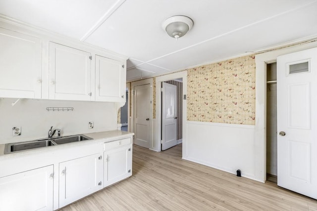 kitchen with a sink, wainscoting, white cabinetry, and light countertops