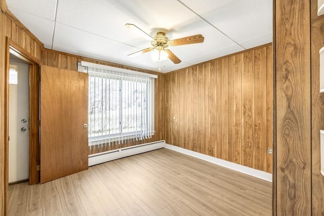 unfurnished room with a baseboard heating unit, wood walls, baseboards, light wood-type flooring, and a ceiling fan