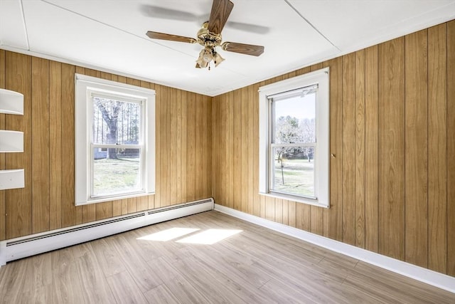 spare room featuring ceiling fan, baseboard heating, baseboards, wooden walls, and wood finished floors