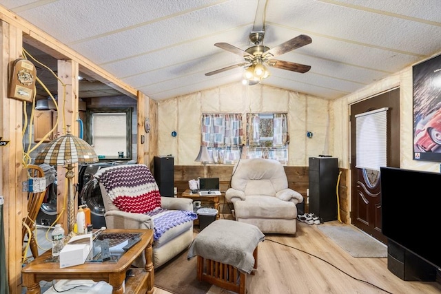 sitting room with lofted ceiling, wood walls, a textured ceiling, light wood-type flooring, and ceiling fan