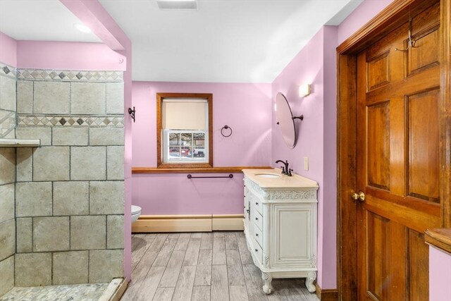 bathroom featuring a baseboard heating unit, vanity, wood-type flooring, a shower, and toilet