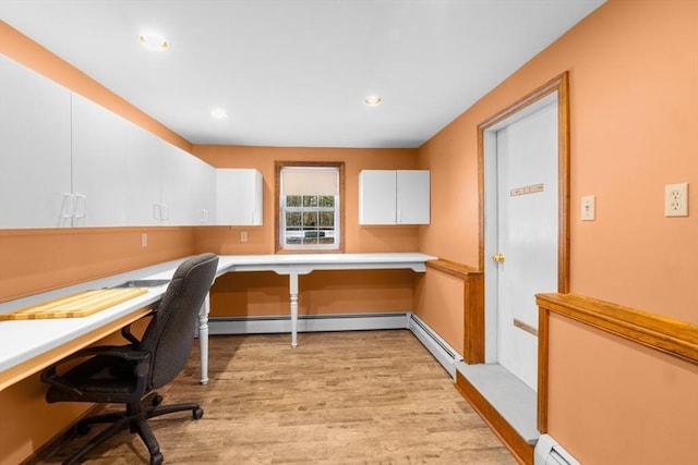 unfurnished office with a baseboard heating unit, built in desk, and light wood-type flooring