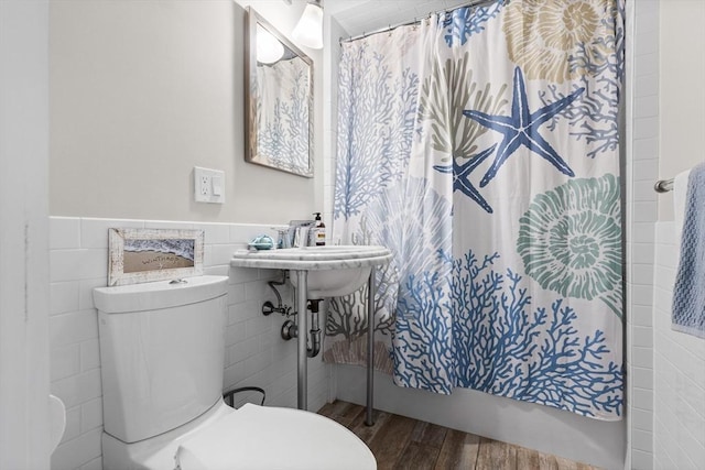 bathroom featuring a wainscoted wall, tile walls, a shower with shower curtain, toilet, and wood finished floors