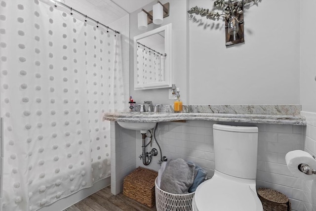 bathroom with tile walls, toilet, shower / bath combo with shower curtain, wainscoting, and wood finished floors