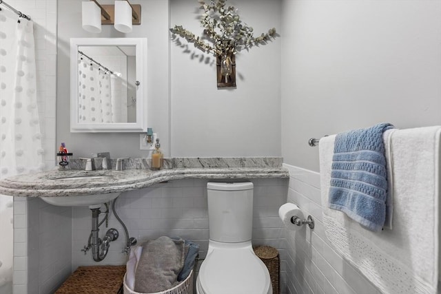 full bath featuring toilet, a wainscoted wall, tile walls, and a shower with shower curtain