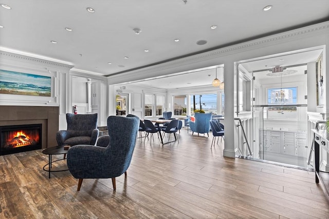 living area with a glass covered fireplace, crown molding, recessed lighting, and wood finished floors