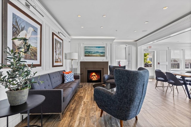 living area featuring a warm lit fireplace, ornamental molding, wood finished floors, and a decorative wall