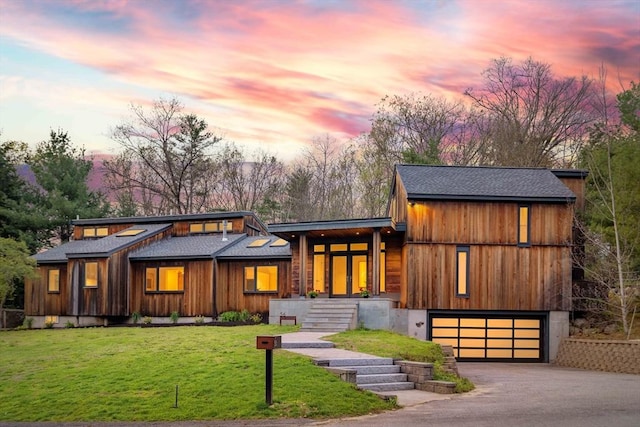 modern home featuring a garage, asphalt driveway, a yard, and roof with shingles