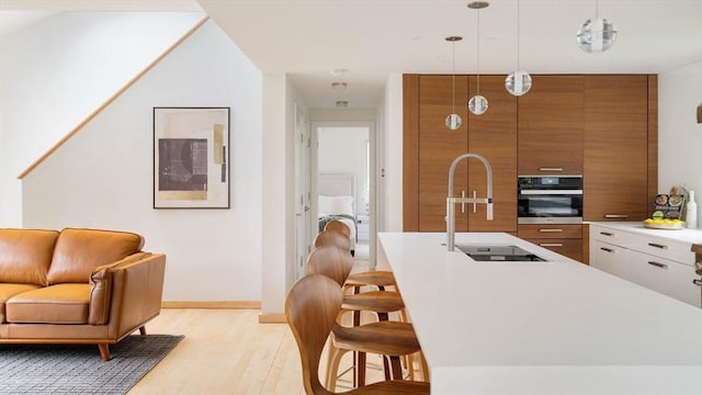 kitchen with oven, brown cabinetry, a sink, modern cabinets, and light wood finished floors