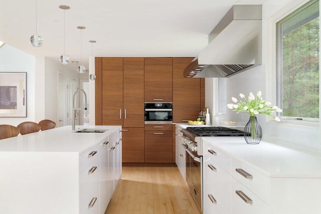 kitchen featuring wall chimney exhaust hood, brown cabinetry, a sink, appliances with stainless steel finishes, and modern cabinets