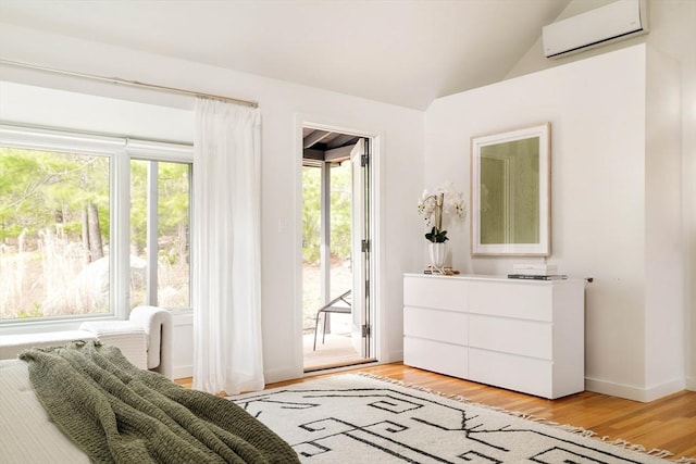 bedroom featuring a wall mounted air conditioner, access to exterior, light wood finished floors, vaulted ceiling, and baseboards