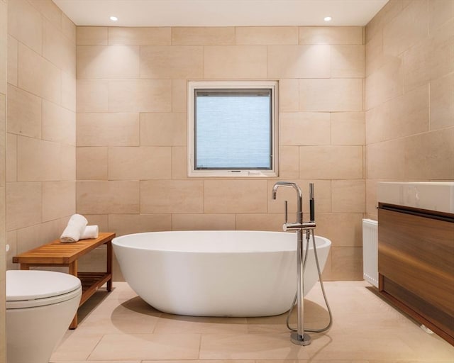bathroom with tile walls, a freestanding bath, tile patterned flooring, toilet, and vanity