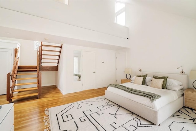 bedroom with light wood-style floors, a high ceiling, and baseboards