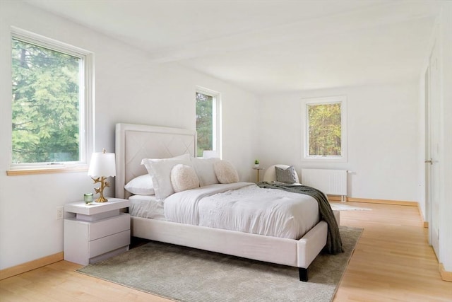 bedroom with radiator heating unit, multiple windows, and light wood-style flooring