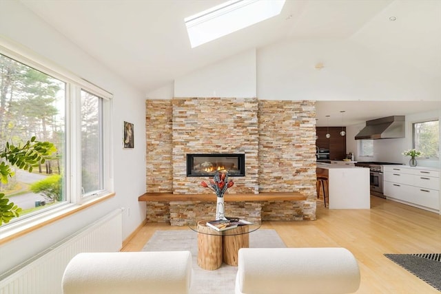 living room featuring radiator heating unit, light wood-style floors, a skylight, a fireplace, and high vaulted ceiling