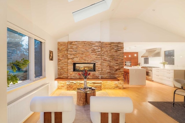 dining room with vaulted ceiling, light wood-style flooring, a stone fireplace, a skylight, and radiator heating unit