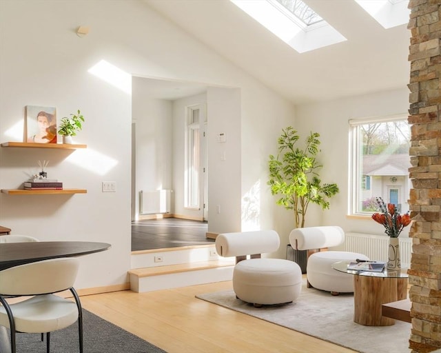 sitting room with wood finished floors, a skylight, vaulted ceiling, radiator heating unit, and baseboards