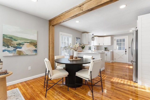 dining space featuring sink, light hardwood / wood-style flooring, and beamed ceiling