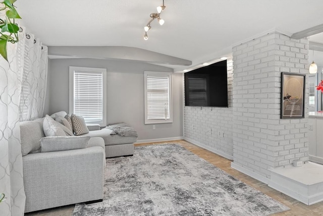 living room featuring track lighting, brick wall, baseboards, wood finished floors, and vaulted ceiling