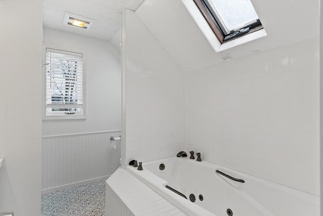 bathroom featuring a jetted tub, vaulted ceiling with skylight, and wainscoting