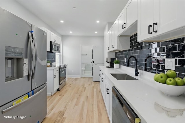 kitchen with a sink, light wood-style floors, stainless steel appliances, white cabinetry, and backsplash