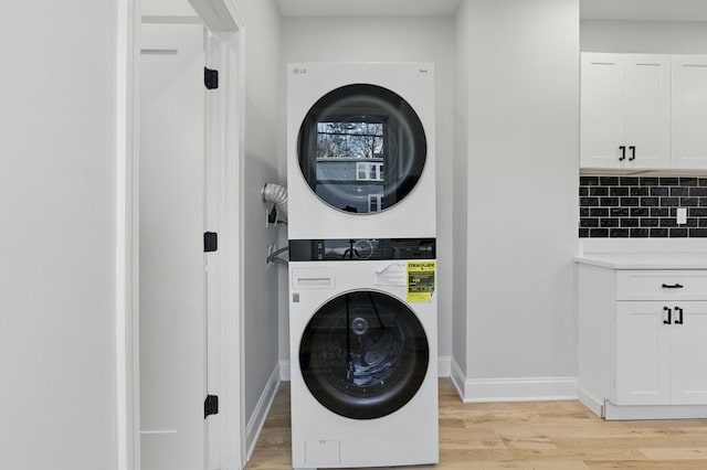 clothes washing area with laundry area, stacked washing maching and dryer, baseboards, and light wood-style floors