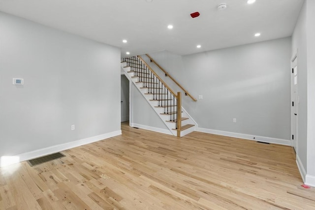 basement featuring visible vents, light wood finished floors, baseboards, and stairway