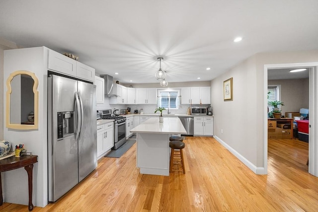 26 Weybosset St, Weymouth, MA 02191 - kitchen featuring stainless steel appliances, wall chimney range hood, a kitchen bar, white cabinetry, and light wood-style floors