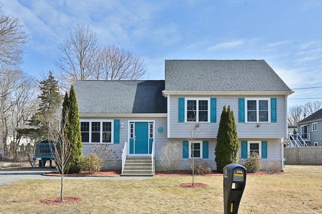 tri-level home featuring a shingled roof, fence, and a front lawn