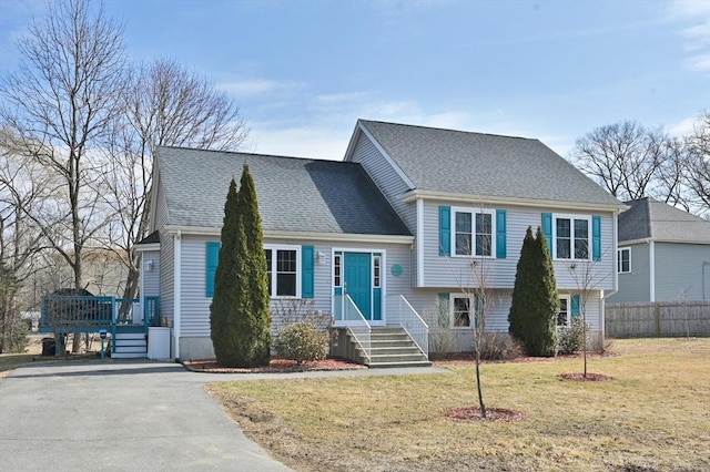 split level home featuring a shingled roof, fence, and a front lawn