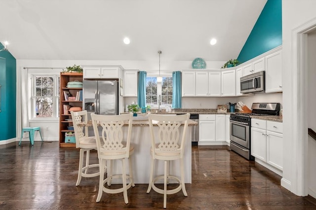 kitchen with stainless steel appliances, lofted ceiling, white cabinetry, and a kitchen island