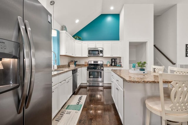 kitchen with appliances with stainless steel finishes, dark wood-type flooring, a sink, and light stone counters