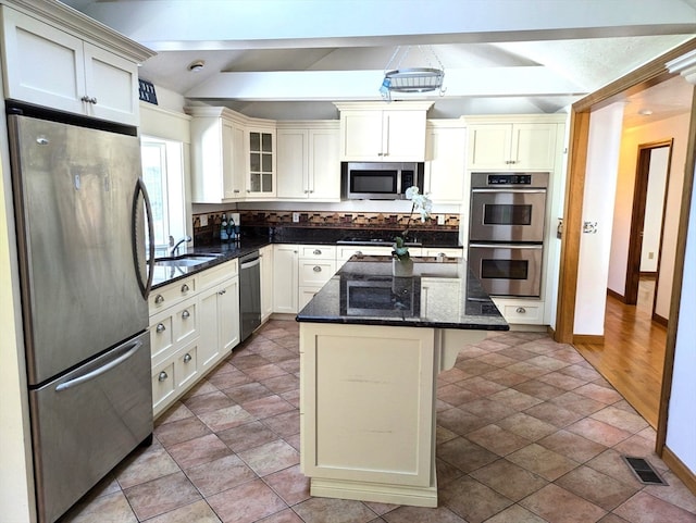 kitchen featuring light wood-type flooring, dark stone counters, stainless steel appliances, a kitchen island, and sink