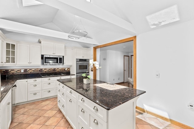 kitchen featuring white cabinets, dark stone countertops, a center island, stainless steel appliances, and lofted ceiling