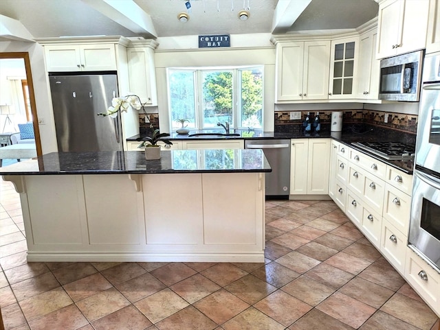 kitchen featuring appliances with stainless steel finishes, dark stone countertops, a center island, and sink