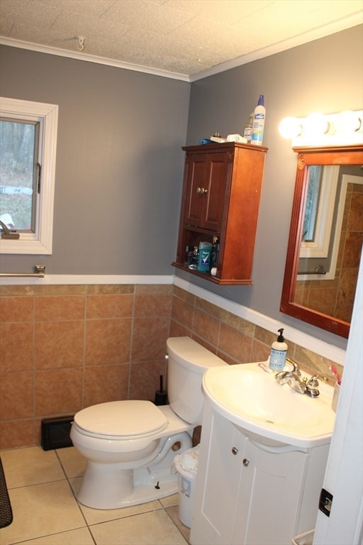 bathroom with tile patterned floors, toilet, vanity, tile walls, and ornamental molding