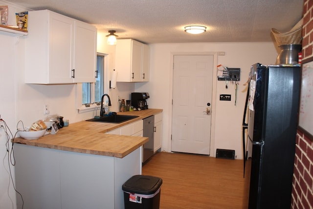 kitchen featuring black refrigerator, wood counters, light wood-type flooring, sink, and white cabinetry