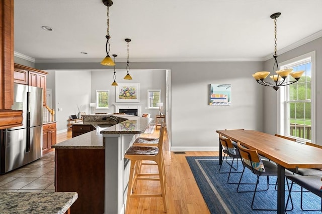 kitchen featuring freestanding refrigerator, a chandelier, a fireplace, baseboards, and crown molding