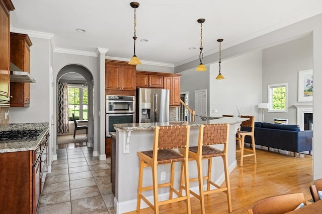 kitchen with appliances with stainless steel finishes, arched walkways, plenty of natural light, a breakfast bar, and crown molding