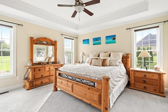 bedroom with a tray ceiling, light carpet, multiple windows, ornamental molding, and baseboards